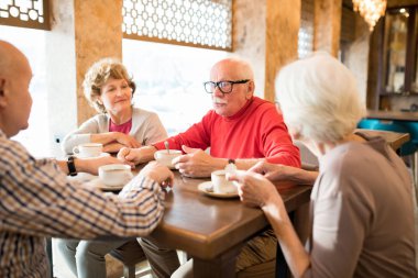 Modern kafede arkadaşlarıyla hikaye paylaşırken gözlük takan ve çay içen bıyıklı yakışıklı yaşlı adam