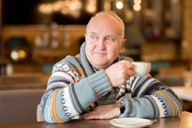 Sıcak kazak içinde içerik tombul olgun adam kafede masada oturan ve sıcak kahve içerken uzağa bakıyor