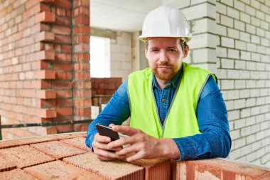 Sitede tuğla duvara yaslanırken kameraya gülümseyen sakallı inşaat işçisiportresi, kopya alanı