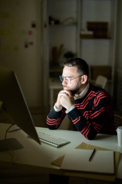 Karanlıkta gece raporu incelerken masada oturan ve ellere yaslanan gözlük ciddi konsantre yakışıklı yönetici