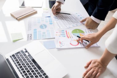 Dizüstü bilgisayar ve kağıtlarla masada duran ve toplantıda pazarlama verilerini tartışan tanınmayan iş arkadaşlarının yakın çekimi: pasta grafiğini işaret eden ve anketin sonucunu açıklayan kadın