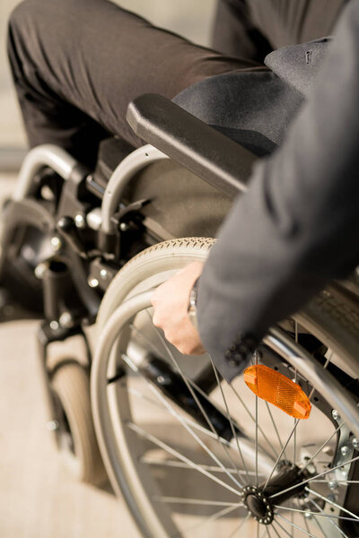 Крупный план бизнесмена-инвалида, сидящего в инвалидном кресле и движущегося по офисному коридору
