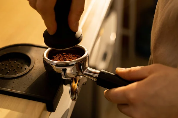 在将研磨咖啡按入 Portafilter 使用篡改机站在柜台处的无法识别的咖啡师的特写镜头 — 图库照片