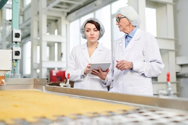 コンベアベルトで立ち デジタルタブレットを使用して食品工場で生産品質検査を行う2人の労働者の肖像画をウエストアップ コピースペース — ストック写真