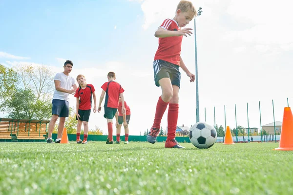 Full length portrait of junior football team training outdoors with focus on  teenage boy leading ball between orange cones, copy space