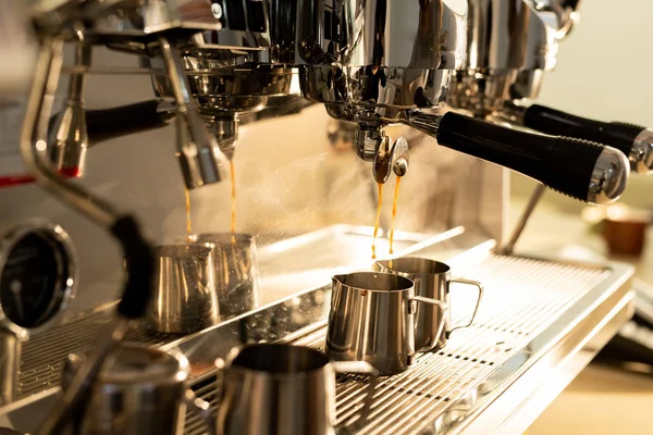 Close-up of modern espresso machine with portafilters brewing strong coffee and pouring it into metal milk jug