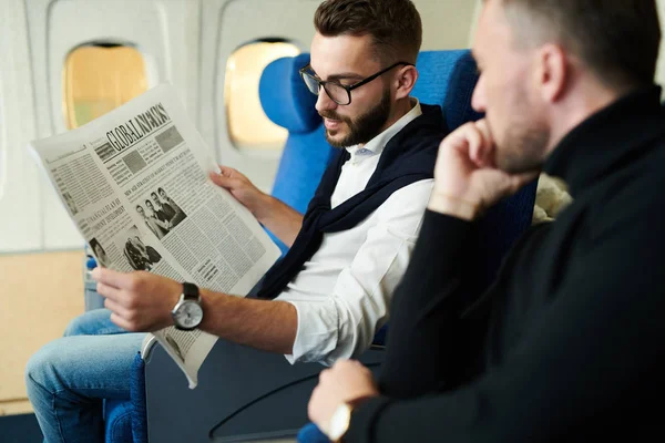 Portrait of two handsome men reading newspaper in plane enjoying long first class flight, copy space