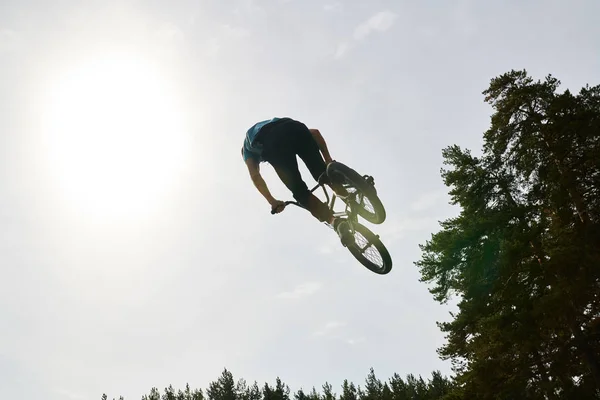 Portrait of unrecognizable young man doing bmx stunts jumping up high against sky, copy space