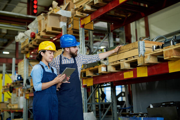 Portrait of two modern factory workers, man and woman, wearing hardhats doing inventory standing by shelves in warehouse, copy space