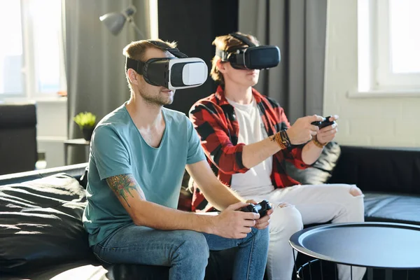 Young friends playing video games wearing virtual reality glasses in their apartment