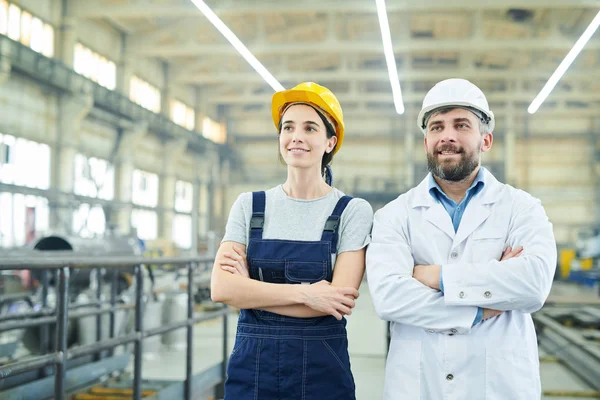 腰上画的两个微笑的工厂工人站在双臂交叉 看着远方 而在工业车间摆姿势 复制空间 — 图库照片
