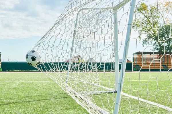Sports background image of football ball in gate net on field outdoors, copy space no people