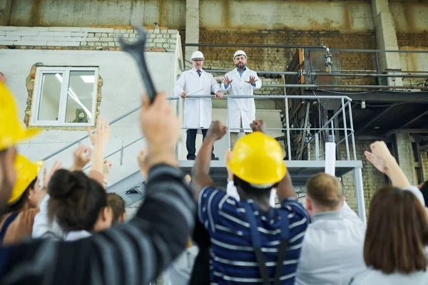 Rear view portrait of multi-ethnic group of workers protesting looking at two factory managers standing at balcony, copy space