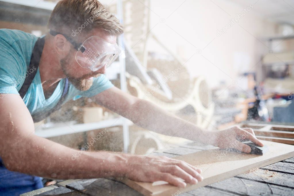 Craftsman in glasses busy with his work, he is using sandpaper in his work