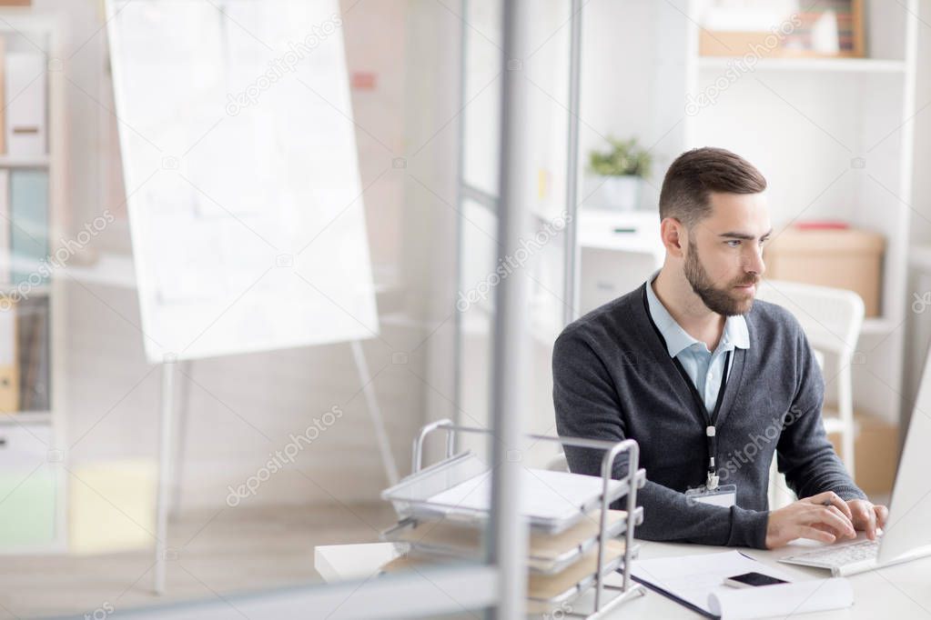 Portrait of bearded businessman using computer while working at desk in modern office, copy space