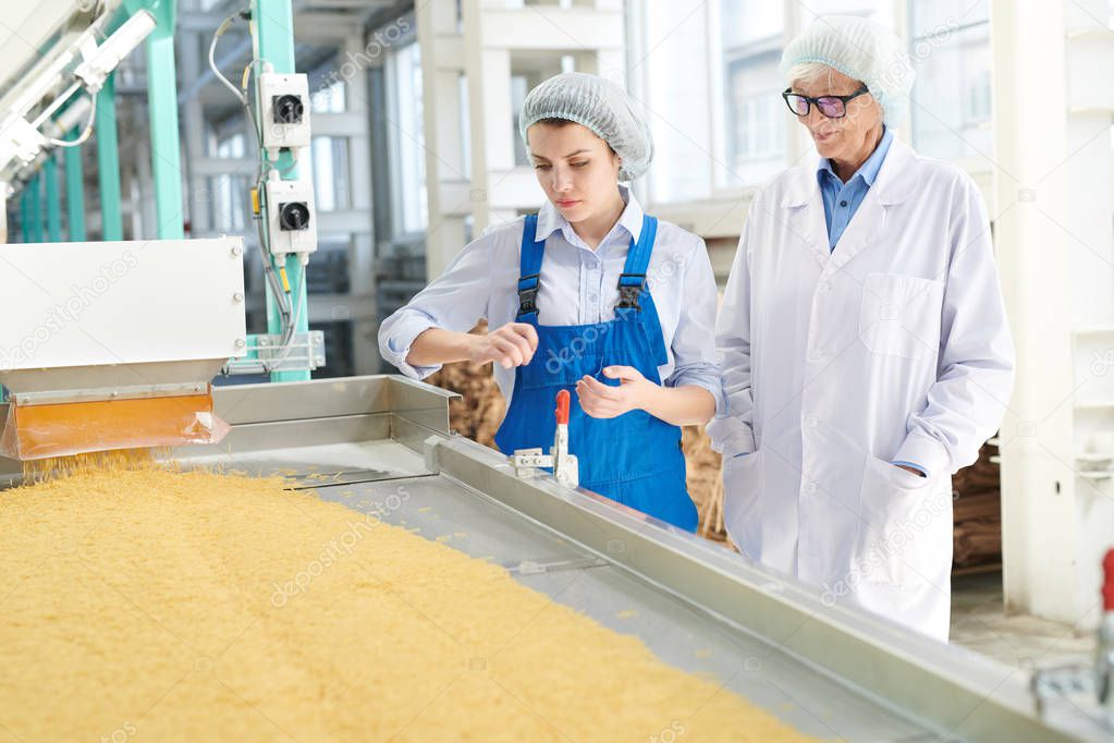 Portrait of two women standing by conveyor belt at modern  food factory, copy space