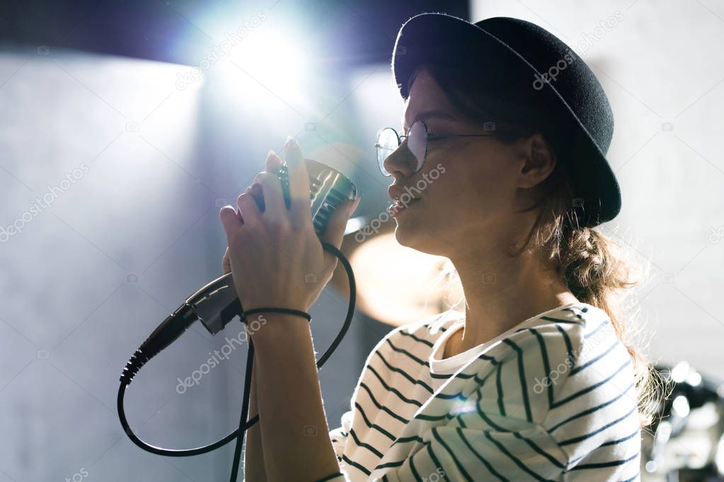Side view portrait of contemporary young woman singing to microphone while performing on stage