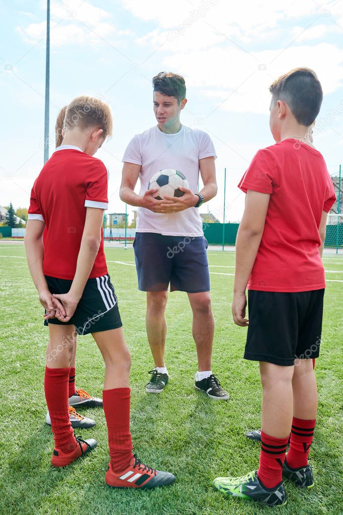 Full length  portrait of smiling coach talking to junior football team giving instructions before match