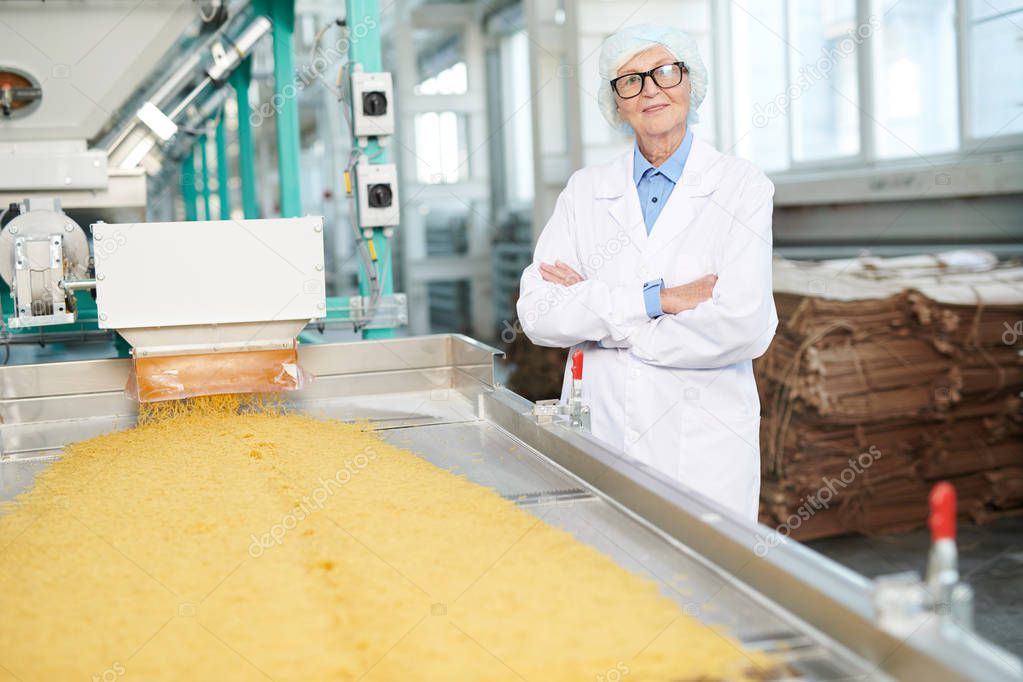 Waist up portrait of  happy senior woman working at factory and posing cheerfully  standing by conveyor belt, copy space