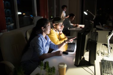 Geceleri karanlık ofiste çalışan birkaç kişinin yan görünüm portresi, ön planda bilgisayar kullanarak iki iş arkadaşına odaklanmak, kopyalama alanı
