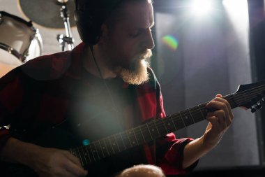 Karanlık prova stüdyosunda gitar çalan yakışıklı sakallı adamın portresi, kopya alanı