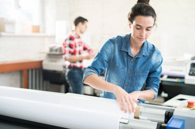 Baskı evinde çalışırken saç topuz yükleme geniş format yazıcı ile ciddi kendinden emin genç kadın