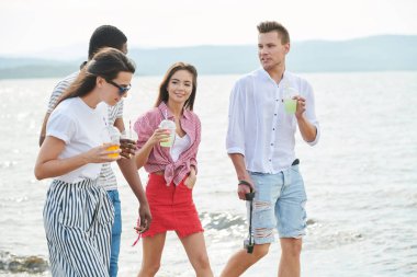 Deniz kenarında yürüyen bir grup gezgin kokteyl içip tatillerini tartışıyorlar.