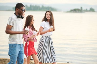 Soğuk içeceklerle genç insanlar zamanlarını dışarıda, gölün kenarında geçiriyorlar.