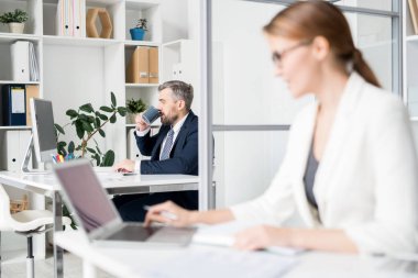 Ciddi dalgın sakallı işadamı resmi ceket masada oturan ve bilgisayar kullanırken kahve içen ve ofiste çalışan