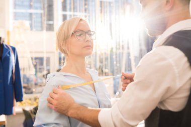 Güneş ışığı ile aydınlatılan geleneksel atölye stüdyosunda giysi montajı yaparken tanınmayan terzi ölçüm kadın müşteri portresi, kopya alanı
