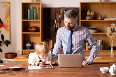 Gömlek ve kravat ciddi yakışıklı baba masada duran ve küçük oğlu, iş davranışı kavramı tablet uygulaması gösteren