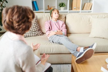 Şapkalı üzgün kayıtsız genç rahat kanepede oturan ve uzak bakarken kollarını geçiş ve terapi oturumunda psikolog soru görmezden