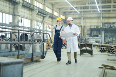 Kadın fabrika işçisinin geniş açılı portresi. Yetişkin bir mühendis ile atölyede yürüme planlarını tartışıyor.