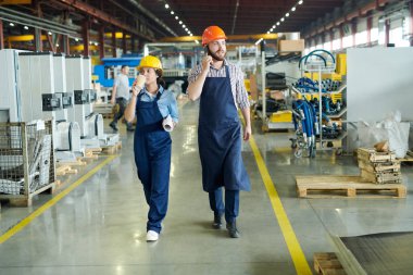 Modern fabrika atölyesi boyunca kameraya doğru yürüyen iki fabrika işçisinin tam uzunlukta portresi