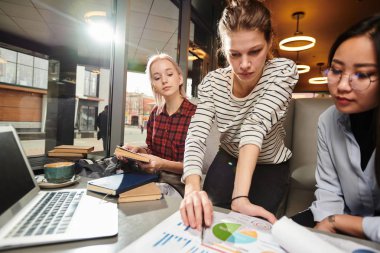 Birlikte ödev yapan üniversite öğrencilerinden oluşan grup, dizüstü bilgisayar ve bazı edebiyat kitaplarını kullanarak grafikleri inceliyorlar.