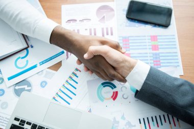 Satış raporları ve analitik kağıtlar ile dolu masada oturan tanınmayan işadamlarının yakın çekim ilerlikleri, müzakere sonrası ortak anlaşmaya varırken el sıkışmak