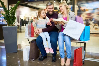 Alışveriş merkezinde mutlu aile alışveriş tam uzunlukta portre ve kağıt torbalar ile bankta oturan, kopya alanı