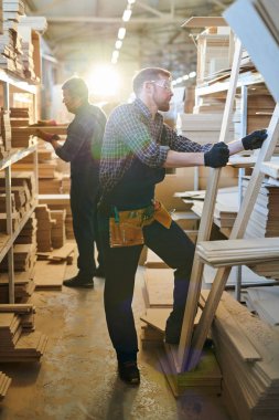 Partikül panoları dolu raflarda ayakta ve depoda montaj için ahşap detayları seçerek üniformalı meşgul assemblers