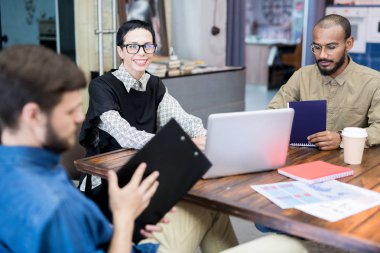 Gülümseyen kadın lider, dizüstü bilgisayar ve çalışanları ile ofiste masada oturuyor
