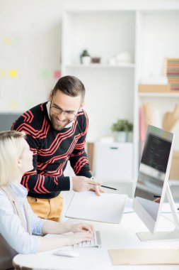 Kodlayıcının çalışmalarını incelerken ve bilgisayar dili kodunu incelerken, çalışan ın masasında duran ve not defteri tutan gözlüklü gülümseyen yakışıklı genç sakallı yönetici