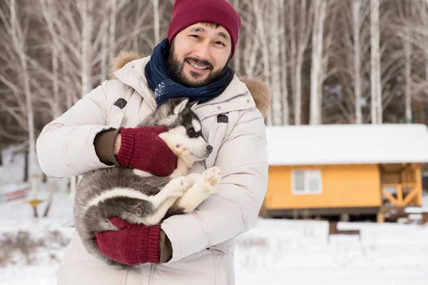 冬に屋外でかわいいハスキー子犬を抱きながらカメラに微笑む現代アジア人男性のウエストアップポートレート コピースペース — ストック写真