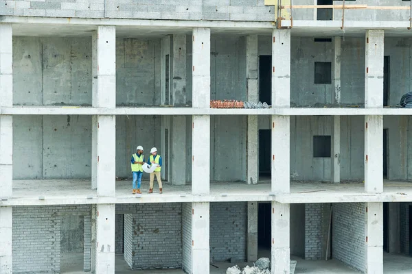 Two men with draft standing on floor of unfinished building on construction site