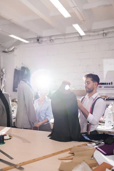 Portrait of handsome tailor fitting formal jackets on mannequins in atelier studio, copy space