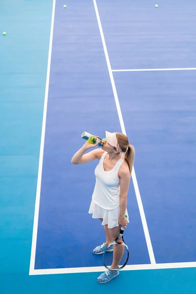 屋内テニスコートでスポーツボトルから水を飲む若いブロンドの女性の高角度の肖像画 コピースペース — ストック写真