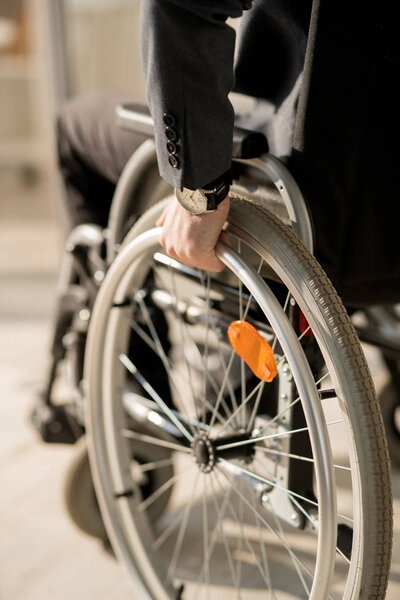 Крупный план инвалида-бизнесмена, кладущего руку на руль, сидящего в инвалидном кресле
