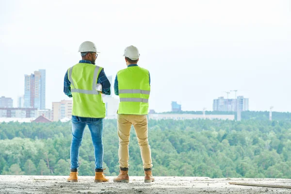 Back View Two Men Hardhats Waistcoats Standing Construction Site Admiring — Stock Photo, Image