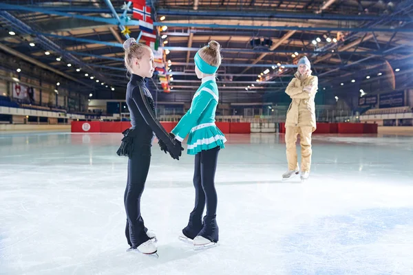 屋内リンクでのパフォーマンス中に2人の小さな女の子フィギュアスケートと手をつないでの完全な長さの肖像画 コピースペース — ストック写真