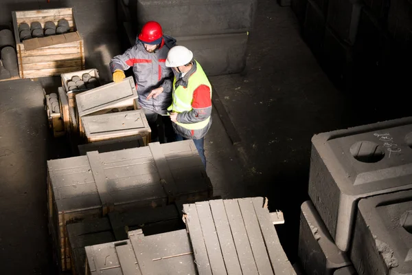 Above view portrait of two factory workers wearing hardhats checking boxes with materials in workshop, copy space