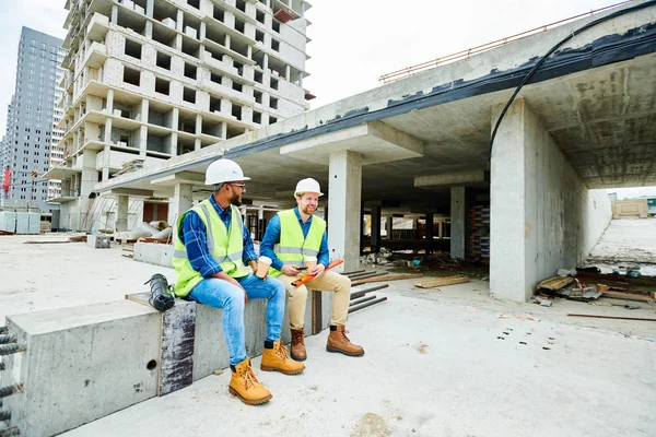 Positieve Knappe Jonge Bouwers Veiligheidsvesten Hardhats Zittend Cement Straal Praten — Stockfoto