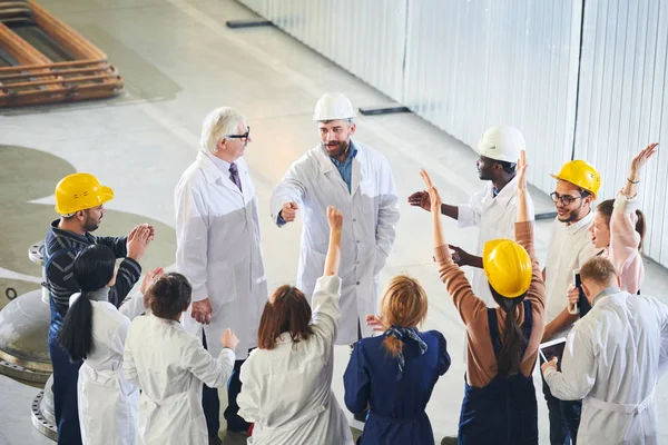 High angle view at group of factory workers protesting emotionally during meeting with management in industrial workshop